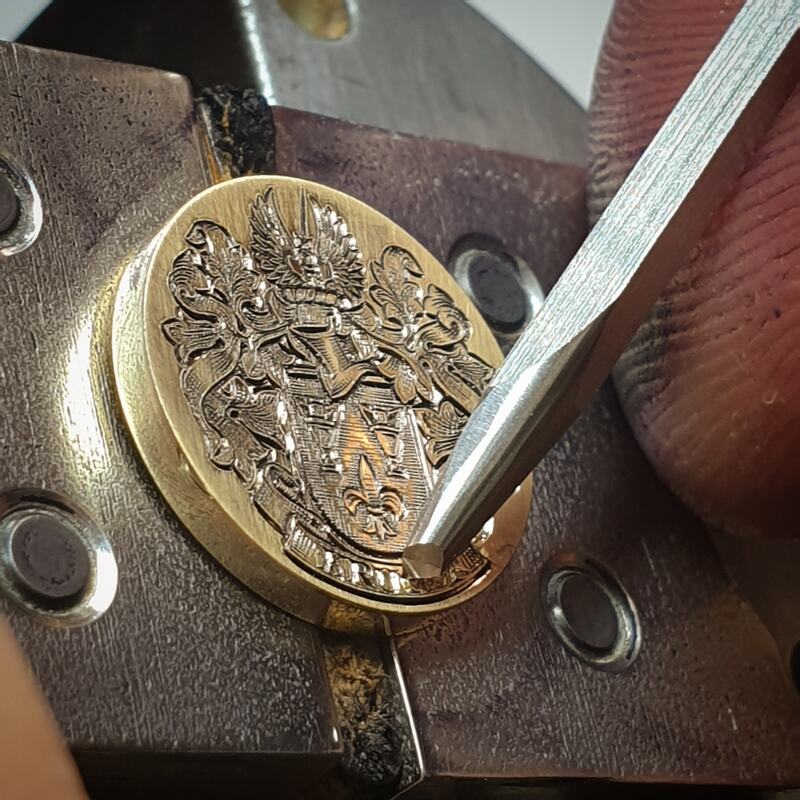 Hand engraving a Coat of Arms onto a round yellow gold cufflink
